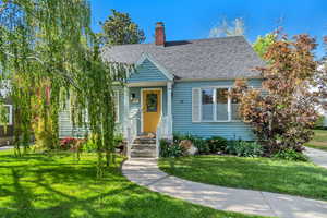 View of front facade with a chimney, a front yard, and a shingled roof