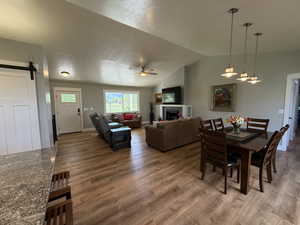 Dining space with ceiling fan, wood finished floors, a barn door, vaulted ceiling, and a fireplace