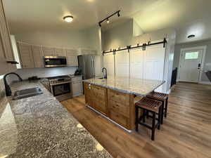 Kitchen featuring stainless steel appliances, a sink, a barn door, decorative backsplash, and vaulted ceiling