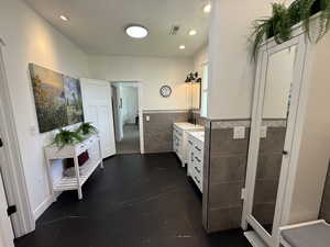 Bathroom featuring tile walls, wainscoting, vanity, and recessed lighting