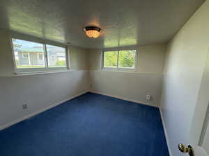 Spare room featuring a textured ceiling, dark colored carpet, and baseboards