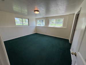 Empty room featuring dark colored carpet, a textured ceiling, and baseboards