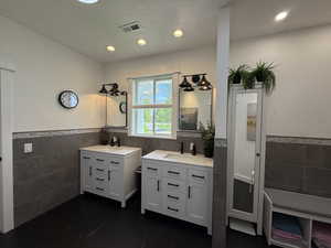 Full bath with tile walls, wainscoting, two vanities, tile patterned flooring, and recessed lighting