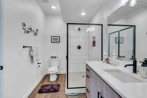 Bathroom with wood finished floors, a stall shower, toilet, and vanity