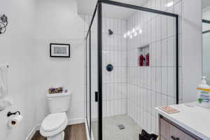 Bathroom featuring a stall shower, toilet, wood finished floors, and baseboards