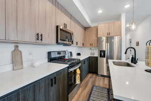 Kitchen featuring stainless steel appliances, a sink, light brown cabinets, light countertops, and light wood-style flooring