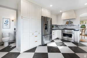 Kitchen featuring high quality appliances, wall chimney range hood, recessed lighting, tasteful backsplash, and white cabinetry