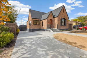 Tudor-style house featuring brick siding, concrete driveway, a shingled roof, an outbuilding, and a detached garage