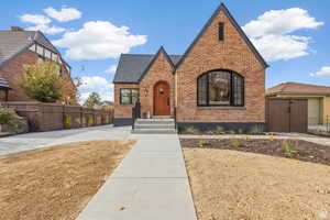 Tudor-style house featuring brick siding, fence, and a shingled roof