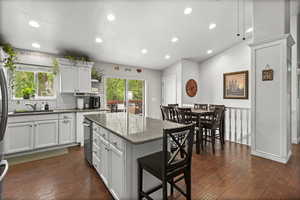 Kitchen featuring dark wood-type flooring, a kitchen island, white cabinets, a sink, and dark stone countertops