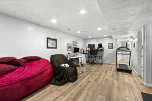 Living room with wood finished floors, a textured ceiling, recessed lighting, and baseboards