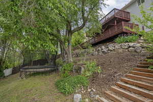 View of yard featuring stairs, a trampoline, and a wooden deck
