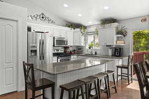 Kitchen with stainless steel appliances, a sink, backsplash, white cabinetry, and a kitchen bar