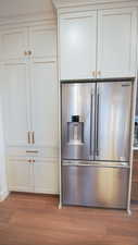 Detailed view of high quality fridge, light wood-type flooring, white cabinetry, and baseboards