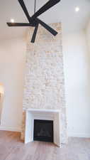 Detailed view of wood finished floors, a stone fireplace, baseboards, a ceiling fan, and recessed lighting