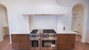Kitchen featuring double oven range, wood finished floors, arched walkways, and light countertops