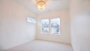 Unfurnished room featuring baseboards, light colored carpet, and a chandelier
