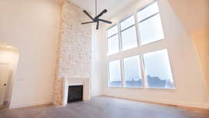 Unfurnished living room with a towering ceiling, a ceiling fan, a large fireplace, plenty of natural light, and wood finished floors