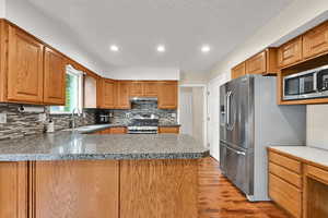Kitchen with stainless steel appliances, a sink, under cabinet range hood, decorative backsplash, and recessed lighting