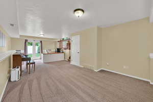 Living room with a textured ceiling, light carpet, an office area, and baseboards