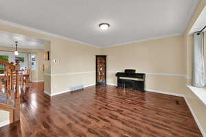 Living room with wood finished floors, baseboards, ornamental molding, and a textured ceiling