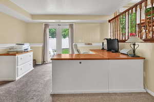 Office space with light carpet, a textured ceiling, and baseboards