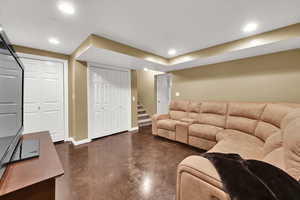 Living area with finished concrete floors, baseboards, stairway, and recessed lighting