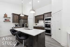 Kitchen with a sink, stainless steel appliances, light wood finished floors, dark brown cabinets, and light countertops