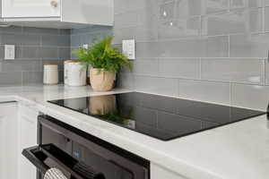 Kitchen view of tasteful backsplash, white cabinetry, light countertops, and induction stove top