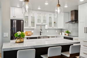 Kitchen with wall chimney exhaust hood, freestanding refrigerator, a sink, a kitchen bar, and recessed lighting