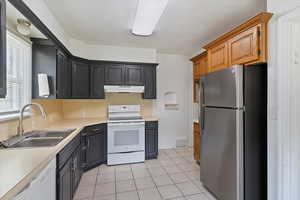 Updated kitchen featuring white appliances, a sink, under cabinet range hood, light countertops, and light tile patterned flooring