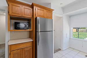 Kitchen featuring freestanding refrigerator, black microwave, light countertops, brown cabinets, and light tile patterned floors