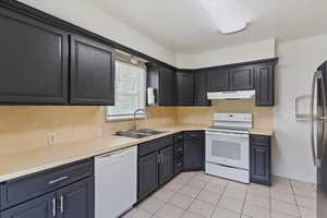 Kitchen with white appliances, a sink, under cabinet range hood, light tile patterned floors, and light countertops