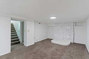 Finished basement family room featuring carpet floors, stairs, and a textured ceiling
