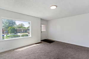 Front room featuring large picture window, carpet, a textured ceiling, and baseboards