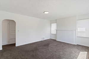 Front room with carpet, a textured ceiling, arched walkways, and baseboards