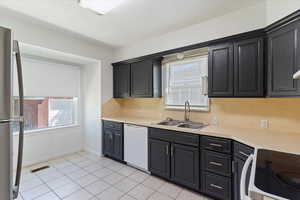 Kitchen featuring a sink, white dishwasher, stainless steel refrigerator, and plenty of natural light