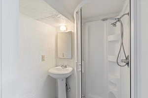 Bathroom featuring a textured wall, walk in shower, and a sink