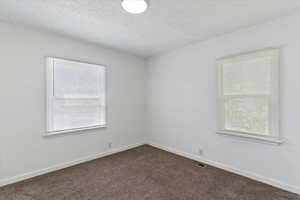 Unfurnished room with dark colored carpet, a textured ceiling, and baseboards