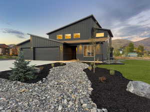 Contemporary house with board and batten siding, concrete driveway, a garage, a mountain view, and a front yard