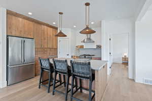 Kitchen featuring high quality appliances, light wood-type flooring, light countertops, hanging light fixtures, and recessed lighting