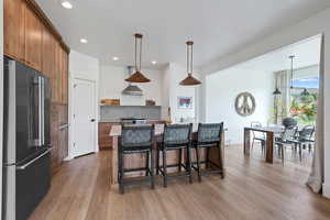 Kitchen featuring high end refrigerator, open shelves, light wood-type flooring, a kitchen bar, and brown cabinetry