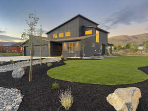 Contemporary house with board and batten siding, driveway, a lawn, a mountain view, and an attached garage