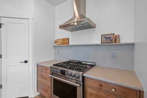 Kitchen with stainless steel stove, wall chimney range hood, brown cabinetry, and light countertops