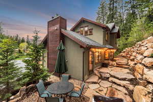 Back of house at dusk with stucco siding, a patio area, a chimney, and a shingled roof