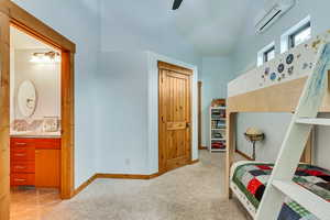 Bedroom featuring a wall mounted air conditioner, light carpet, connected bathroom, baseboards, and a sink