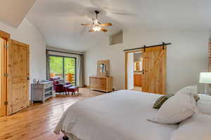 Bedroom featuring a barn door, lofted ceiling, light wood-style flooring, ceiling fan, and connected bathroom
