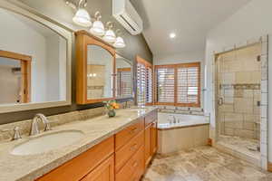 Bathroom with an AC wall unit, a bath, a stall shower, and double vanity