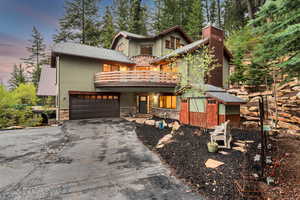View of front of home featuring a balcony, asphalt driveway, stone siding, a chimney, and an attached garage