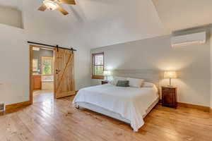 Bedroom with a wall mounted air conditioner, a barn door, light wood finished floors, baseboards, and ensuite bath